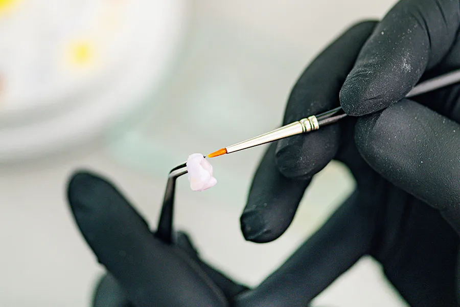 Técnico caracterizando con un pincel una corona dental de cerámica